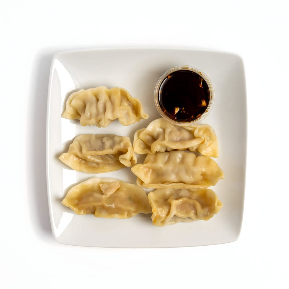 Six steamed dumplings arranged on a white square plate with a side of soy dipping sauce.