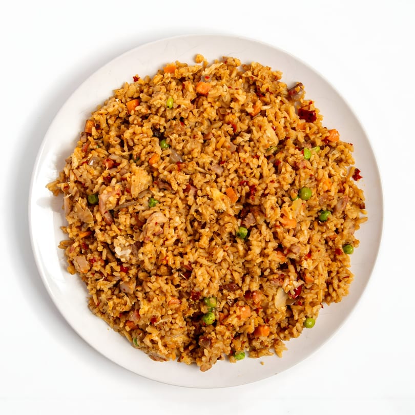 Overhead view of a white plate filled with chicken fried rice, peas, and carrots.