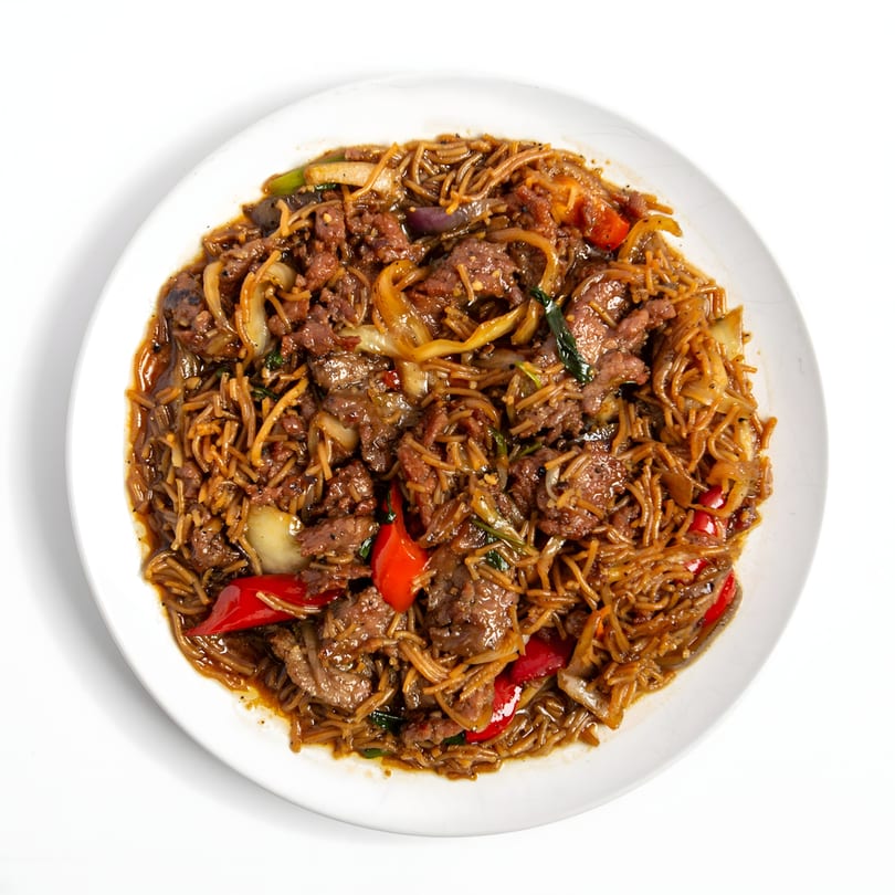Asian beef and noodle dish with red bell peppers and onions on a white plate.