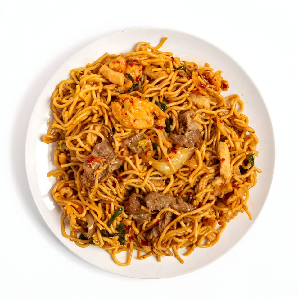 A white plate holds a generous serving of Asian noodles with chicken, beef, and vegetables.