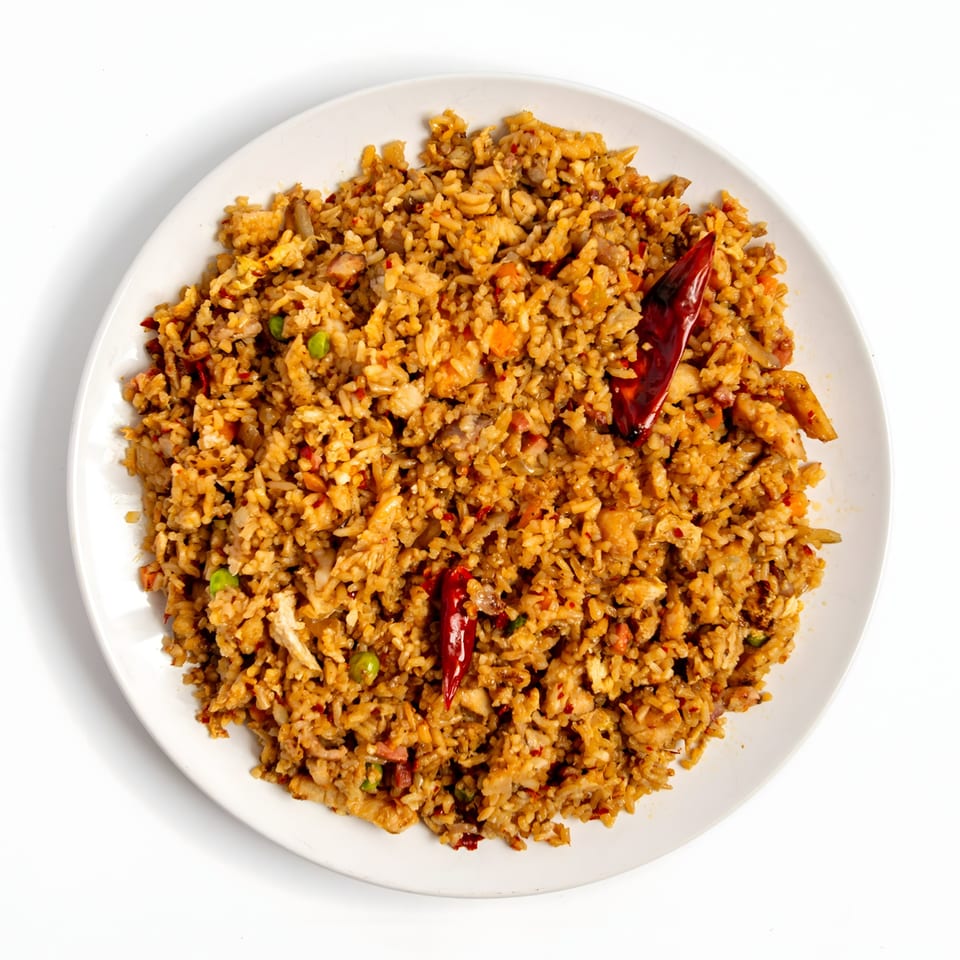 Spicy Asian fried rice with chicken, vegetables, and dried red chilies on a white plate.
