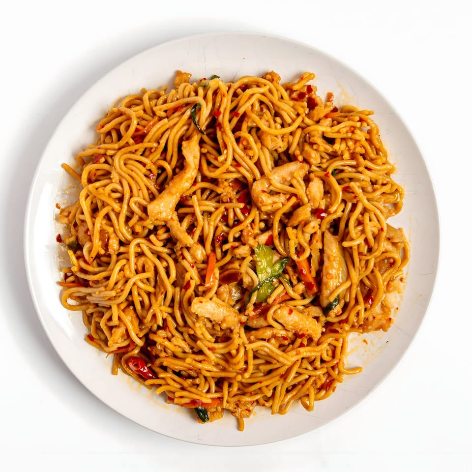 Overhead view of a white plate filled with Asian noodles, chicken, and vegetables.